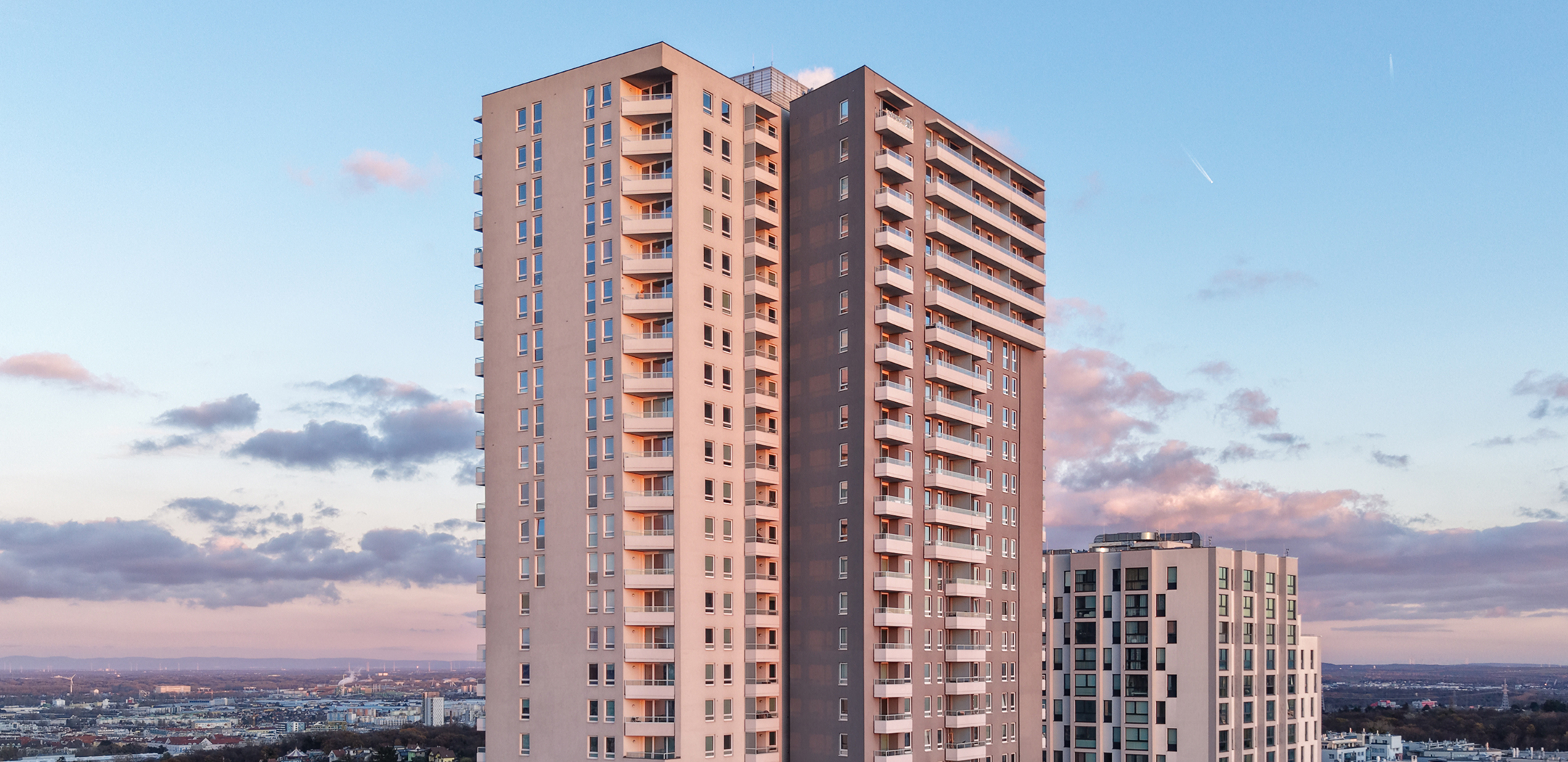 Weitwinkelansicht der oberen Stockwerke eines modernen Hochhauses vor einem Abendhimmel.