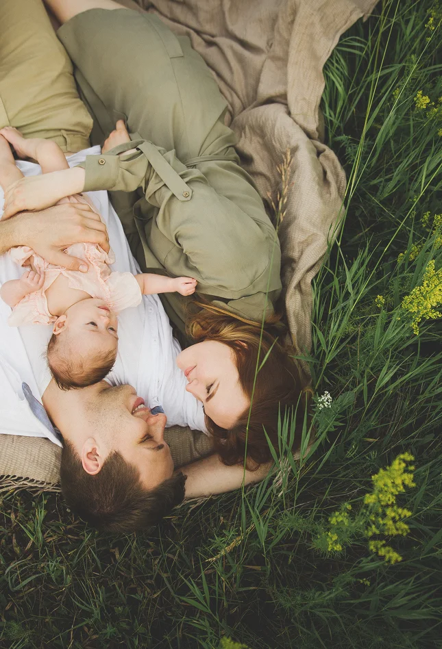 Eine Familie liegt entspannt auf einer Picknickdecke im hohen Gras.